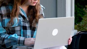 zuversichtlich lächelnd Frau funktioniert draußen, Typen auf Laptop. Schüler tut ihr Hausaufgaben Projekt auf Computer, Sitzung auf Straße. video