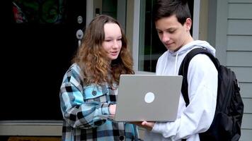 boy shows something on laptop of girl she corrects mistakes she smiles a briefcase loser first relationship boy teenager clothes autumn spring near the house at door to come to friend to help video