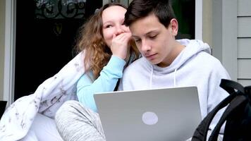 Söt flicka viskande hemlighet i öra av henne skrattande vän i de händer av en dator sitta på veranda omslag själv med en filt skratt vänliga hälsningar tonåringar kommunicera vänskap begrepp video