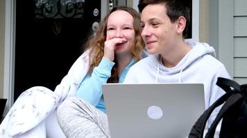 Pretty girl whispering secret in ear of her laughing friend in the hands of a computer sit on porch cover yourself with a blanket laugh sincerely teenagers communicate friendship concept video