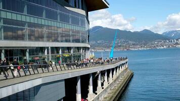 du kan ser de staty av en släppa från de pacific hav restauranger kaféer glas kontor byggnad bergen vit moln människor gående längs de vägbank fiskmås flygande i de himmel hamn kanada plats video