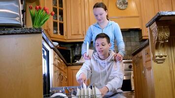 Amerikaans jong jongen en meisje aan het doen huiswerk samen afvegen schoon smaakpapillen na avondeten in modern keuken. gelukkig paar aan het doen huis klusjes samen video