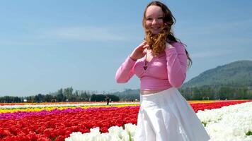 bellissimo giovane ragazza nel bianca tulipani sta sorridente regola sua capelli contro il cielo montagne bianca tennis gonna rosa camicetta spazio per testo primavera bellezza gioventù leggero video