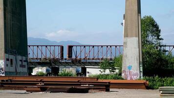 Pattullo Bridge over Fraser River train passing under bridge. close-up shot from technological site scattered iron beams for the construction of new bridge against the backdrop of mountains and sky video