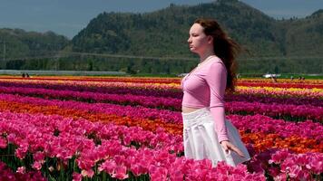 Young woman tourist in pink dress and straw hat standing in blooming tulip field. Spring time video