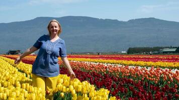 adulto mujer en campo de tulipanes ropa azul amarillo me gusta bandera de Ucrania alegría felicidad en montañas floreciente amarillo flores libertad frescura aire amarillo pantalones azul blusa rubio ordinario hembra video
