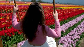 een meisje spelen in een bloem tuin rijden Aan een schommel haar- ontwikkelt roze blouse van een Europese meisje wit rok video