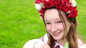 beautiful Ukrainian young woman tender girl in a large red wreath of bright pink white red flowers braiding ribbons in hair wind tenderness cleanliness peace in Ukraine Peacetime people Real life video