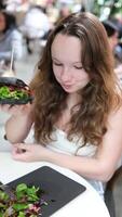 ung tonåring flicka i en vit topp vit europeisk kvinna äter i ett dyr restaurang skön saftig svart burger utsökt mat kalorier. dålig näring restaurang annons smörgås svart vit video