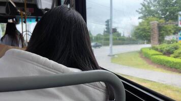 onherkenbaar meisje met haar terug naar de camera voorbijgaan door een bus hou op in een klein stad- auto's het rijden regen donker haar- capuchon video