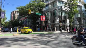 canadense amarelo Táxi às a encruzilhada animado rua cidade vida pessoas cruzando estrada motociclista tráfego luz edifícios dentro Vancouver Canadá 2023 video