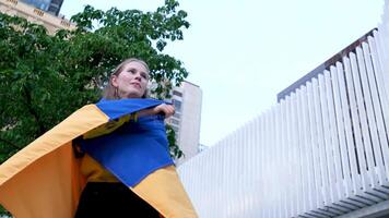 cerca arriba contento joven ucranio mujer envolver en un nacional bandera azul y amarillo. luz de sol alrededor. cosecha. Ucrania, independencia, libertad. patriota símbolo, victoria en guerra. lento movimiento video