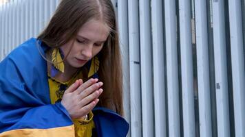 vrouw met oekraïens vlag Aan schouders bidt handen gevouwen in voorkant van borst blond haar- inschrijving schoonheid jeugd pijn in hart oorlog in land Oekraïne zullen winnen verwachting gebed verzoek naar god ik willen vrede video
