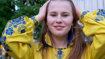beautiful young girl straightens her blond hair yellow blouse with blue embroidery earrings bird feathers yellow and blue gentle smile outdoors video