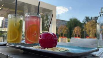 citron boisson et Orange boisson sur le été terrasse près une délicieux mousse dessert dans le forme de une grand pétiole sur amande feuilles à l'extérieur ayant petit déjeuner dépenses temps ensemble video