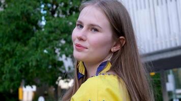 jong mooi vrouw, jong meisje in groot stad in geel geborduurd shirt, geborduurd blouse, lang bruin haar, glimlach, veer oorbellen, geel en blauw kleuren in kleren, oekraïens nationaal kostuum video