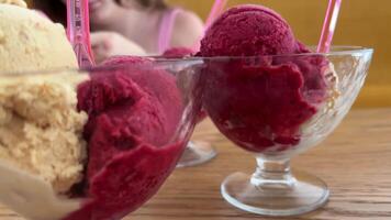 A girl is filming stories in the background on her phone. Closeup pan of raspberry sorbet ice cream balls on wooden table video