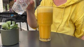 delicious orange juice with ice hot day on a gray table female hand pours pieces of ice into a freshly squeezed multifruit drink slow motion Small flowerpot beautiful serving in Corfu island video