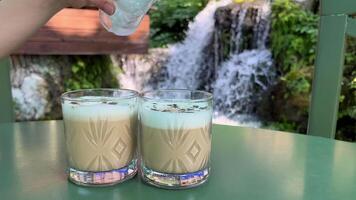 Lägg till is kuber till cappuccino glas glasögon mot de bakgrund av en vattenfall i albania resa turister bekvämlighet skön se semester video