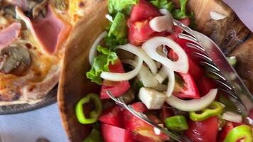 Grieks salade wezen geserveerd op een bord door een salade lepel met pizza met vlees en champignons in een van de restaurants in albanië. uien, tomaten, komkommers, kaas en peper. video
