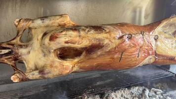 Roasting whole lamb on a spit metal rotating stick over fire, golden crispy skin, lamb bbq grill, 4K shot video
