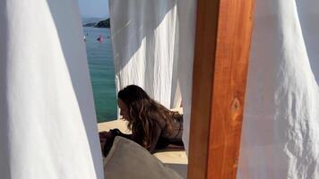VIP bord de mer vacances dans Albanie dans premier ligne hamac plus de l'eau Jeune fille dans noir paréo marcher lent mouvement dans mains de téléphone génial Passe-temps se détendre marcher le long de promenade blanc des puces plus de transats video