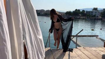 VIP playa vacaciones en Albania en primero línea hamaca terminado agua joven niña en negro pareo caminar lento movimiento en manos de teléfono genial pasatiempo relajarse caminar a lo largo paseo blanco pulgas terminado hamacas video