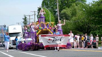 Cloverdale female representatives wearing purple beauty queen clothes riding huge truck down street waving hands gay parade performance crown head flag parade down the street of vancouver surrey video