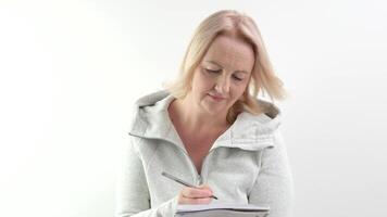 haciendo planes para el futuro escritura en un cuaderno con un bolígrafo, mujer en un blanco antecedentes escribe abajo ideas planes para el día de compra, decisiones a pensar, aumento su cabeza, Mira dentro el marco video