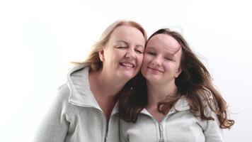 a woman and a girl hugging leaning their cheeks against each other look into the frame pull lips for kiss mom and daughter on white background identical clothes close eyes from pleasure tenderness joy video