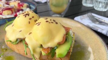 Healthy morning food. eggs Bendict on brioche buns with lightly salted salmon and cream with cheese beautiful serving in a restaurant hollandaise sauce and spinach on english muffin. Close up video