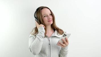 girl with headphones and a mobile phone at a photo shoot studio white background keep a finger on the headphones make eyes pose mobility music listen track sportswear play sports video