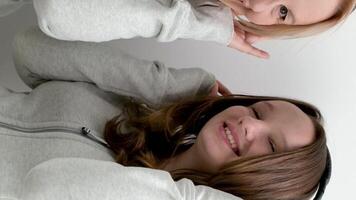 Mutter und Tochter im identisch Sport Sweatshirts grau Farbe auf ein Weiß Hintergrund im Kopfhörer Hören zu Musik- Herstellung Augen lächelnd beim jeder andere Licht europäisch Frauen singen entlang video