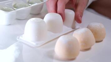 différent les saveurs de asiatique dessert mochi, une femme main prend en dehors sucré la glace crème fabriqué de pois et riz amidon pâte de une boîte sur une blanc assiette video