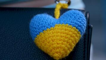 a keychain in the shape of a knitted heart is attached to a handbag and a Ukrainian flag video