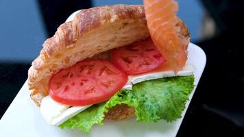 Croissant sandwich with cream cheese, salmon and arugula on a white plate, gray background, close-up. Healthy breakfast concept video