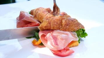 prik met een vork en besnoeiing met een mes heerlijk croissant met ham en kaas geplaatst Aan wit bord croissant met prosciutto en kruiden video