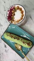 Hot lattes with foam Eclair with pistachios French pastry eclairs with pistachio cream filling covered with green glaze circle rotation close up top view video