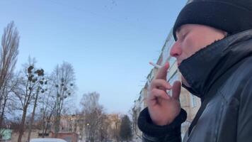 närbild isolerat porträtt av man vem röker en cigarett och släpps rök in i de kamera lins. skäggig medelålders man med dålig vanor röker på de gata på vinter- dag. video