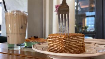 honing taart eigengemaakt okkernoot en amandel taart is besnoeiing met een lepel Aan een keramisch bord Aan wit houten achtergrond. kant visie, dichtbij omhoog. video