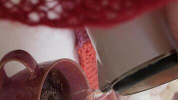 POV pouring black tea into a pink mug on a white wooden table at cafe. video