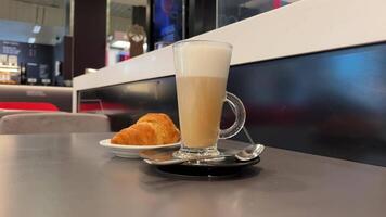 een Frans croissant en een kop van cappuccino Aan een zwart bord. detailopname met langzaam beweging. omwenteling in een cirkel. wit achtergrond. video