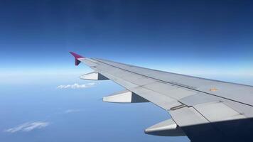 vinge av ett flygplan flygande ovan vit moln mot blå himmel se genom ett flygplan fönster. video