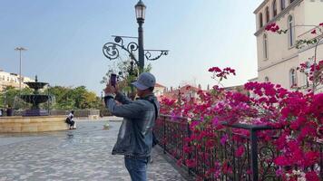 zonsondergang stad- phu quoc Vietnam 25.02.2024 mannetje toerist in denim pak en pet duurt afbeeldingen van bezienswaardigheden Aan mobiel telefoon. snel wezen ontwikkelde Europese stad kopiëren. verbazingwekkend toekomst toevlucht, kien Giang provincie video