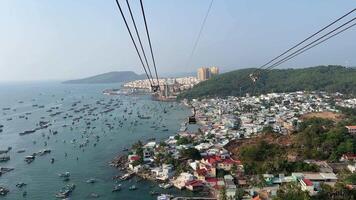 Ships at sea long cable car above mountain on island in sunset and old fishing town below under cloudy blue sky in Phu Quoc island Vietnam video