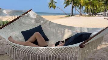 Woman using mobile phone in a hammock on the beach video