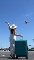 un joven hermosa niña en un blanco vestir y un sombrero con un maleta olas su mano a un volador avión viaje vacaciones alegría saltar tener divertido perder el avión prisa a salir un nuevo oportunidad en vida video