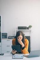 Portrait of tired young business Asian woman work with documents tax laptop computer in office. Sad, unhappy, Worried, Depression, or employee life stress concept photo