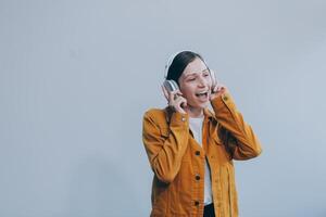 The beautiful emotional European brown-haired woman with healthy clean skin, charming smile, dressed in casual light clothes, listens and enjoys music on headphones with tablet on a white background. photo