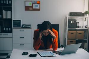 Portrait of tired young business Asian woman work with documents tax laptop computer in office. Sad, unhappy, Worried, Depression, or employee life stress concept photo